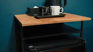 A small wooden table with a black tray holding a black coffee maker, a white mug, and a black box.