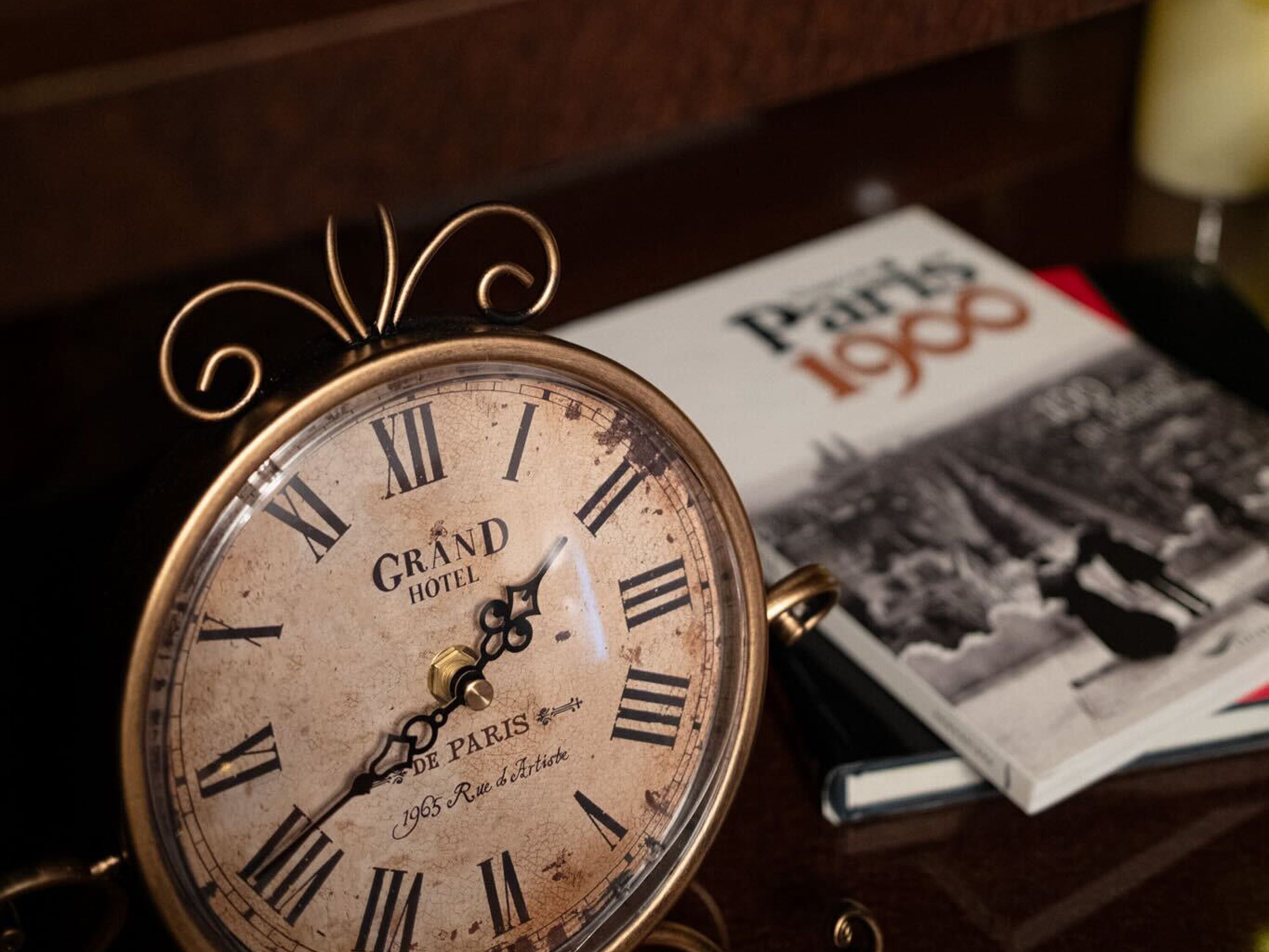 Un reloj antiguo del Grand Hotel Paris con números romanos y diseño de latón, sobre una mesa con una revista.