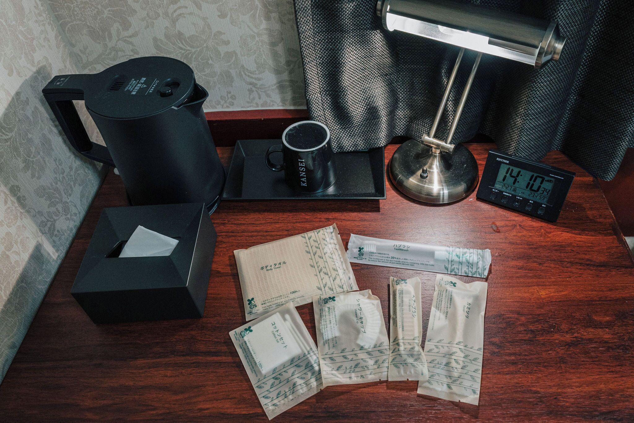 A wooden table with a coffee maker, a mug, a clock, and several tissue packets.