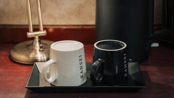 Una bandeja con una taza blanca, una taza negra, una cafetera y una lámpara sobre una mesa.