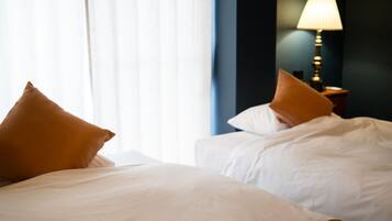Camera d'albergo con due letti, biancheria bianca e una lampada sul comodino.