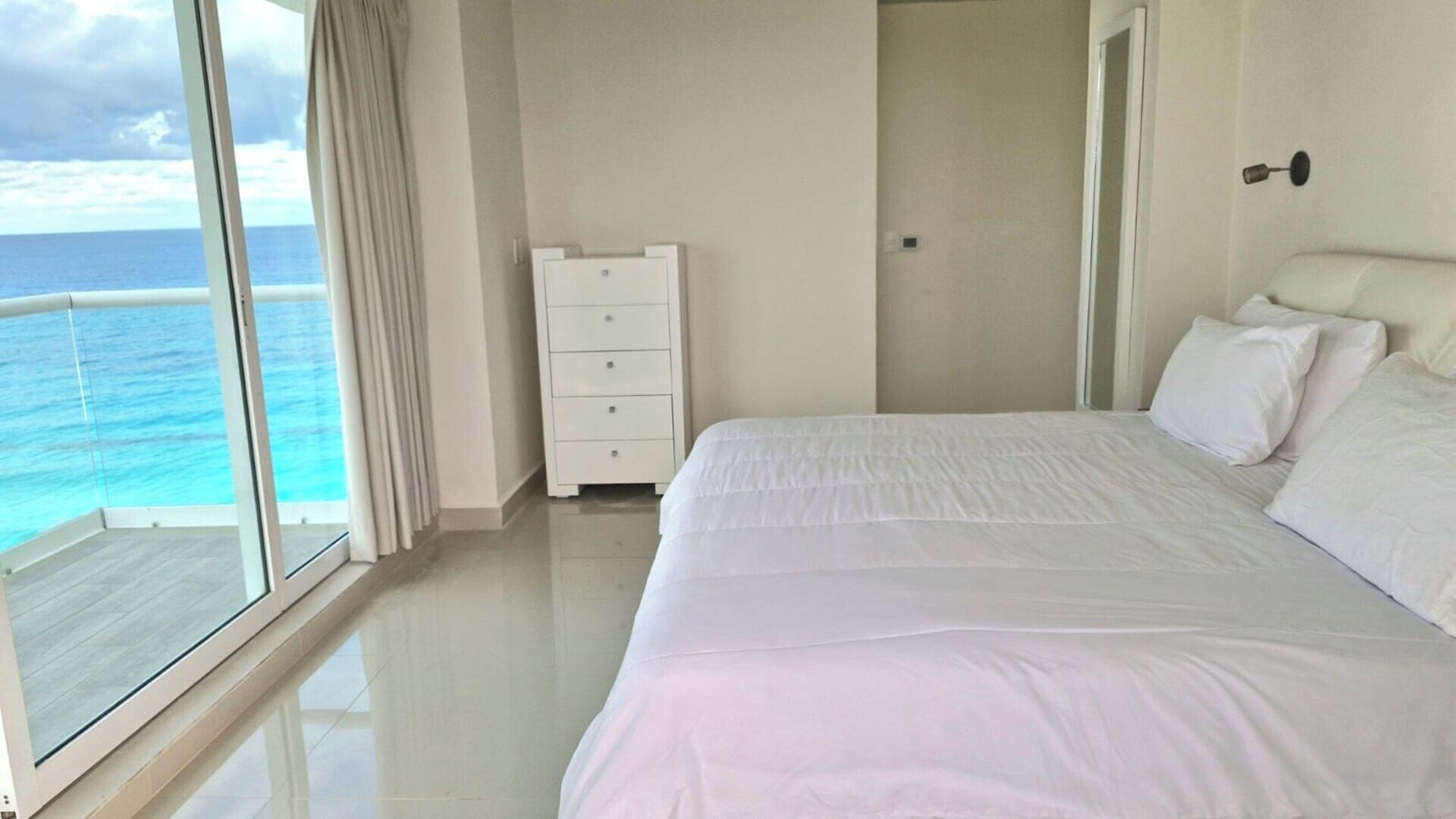 A bedroom with a large bed, a dresser, and a view of the ocean.