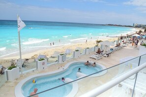 A resort pool area with a view of the beach, lounge chairs, and a flag.