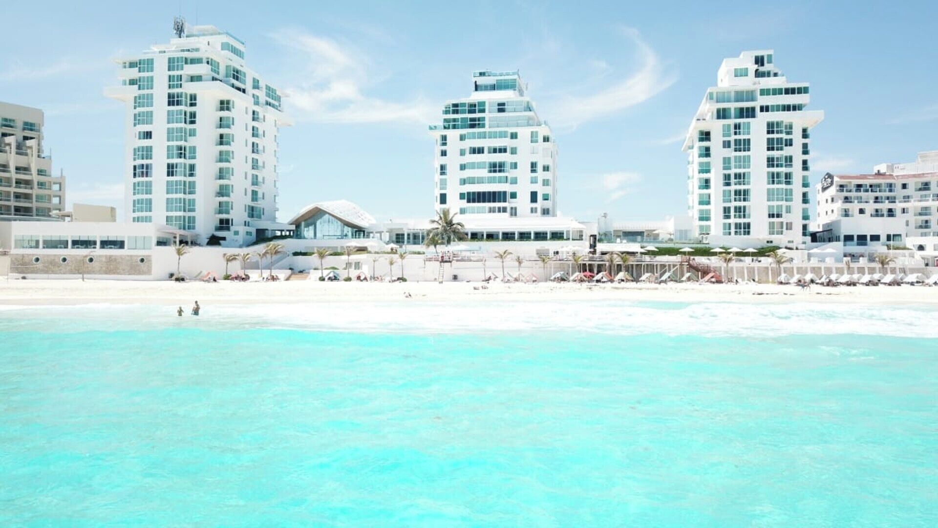 A beachfront hotel with multiple high-rise buildings, a sandy beach, and clear turquoise waters.