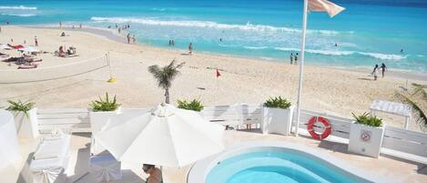 A pool area with lounge chairs and umbrellas, overlooking a beach with people and a lifebuoy.
