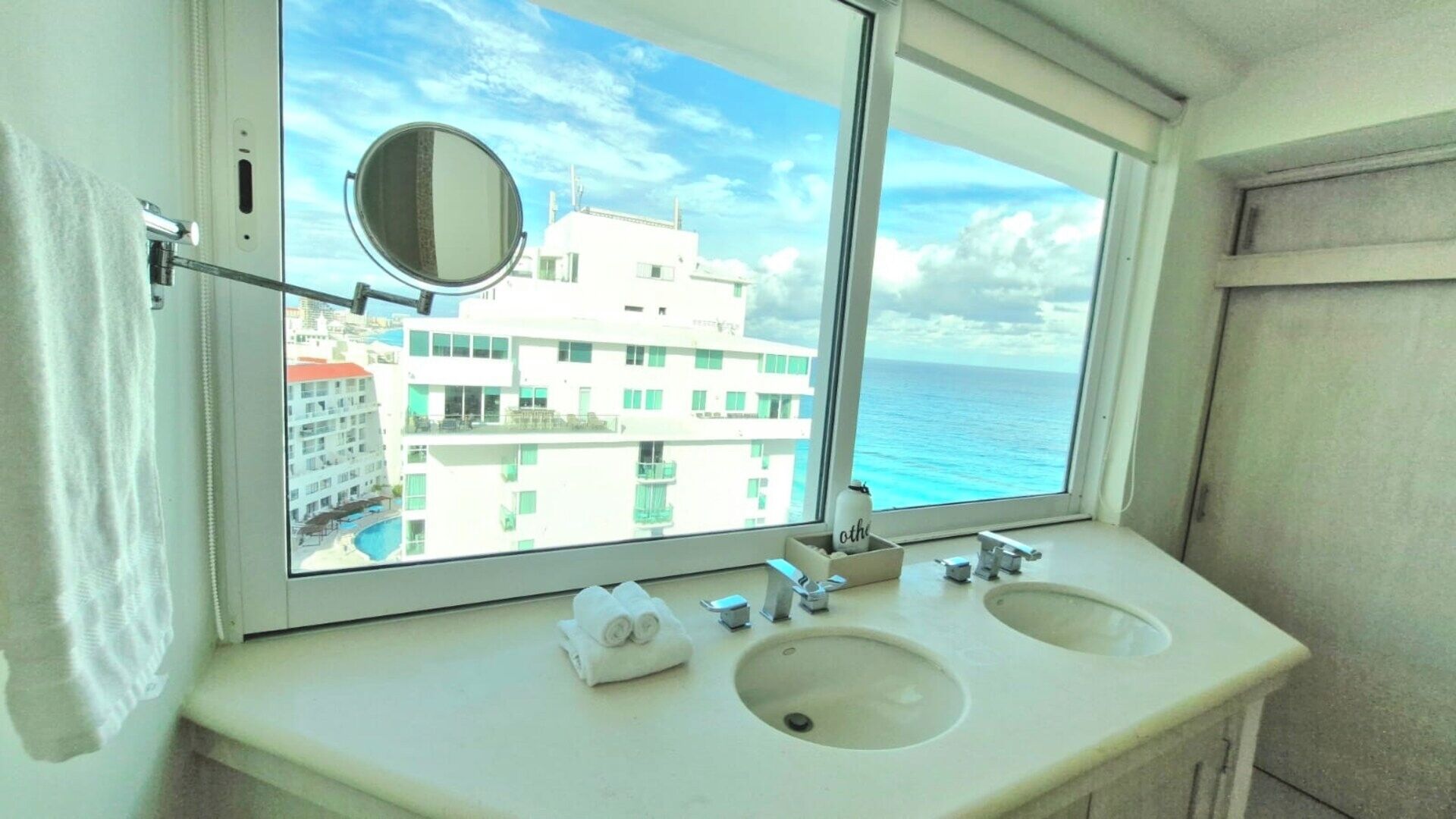 Casa de banho com duas pias, um espelho e uma janela com vista para um edifício e o mar.