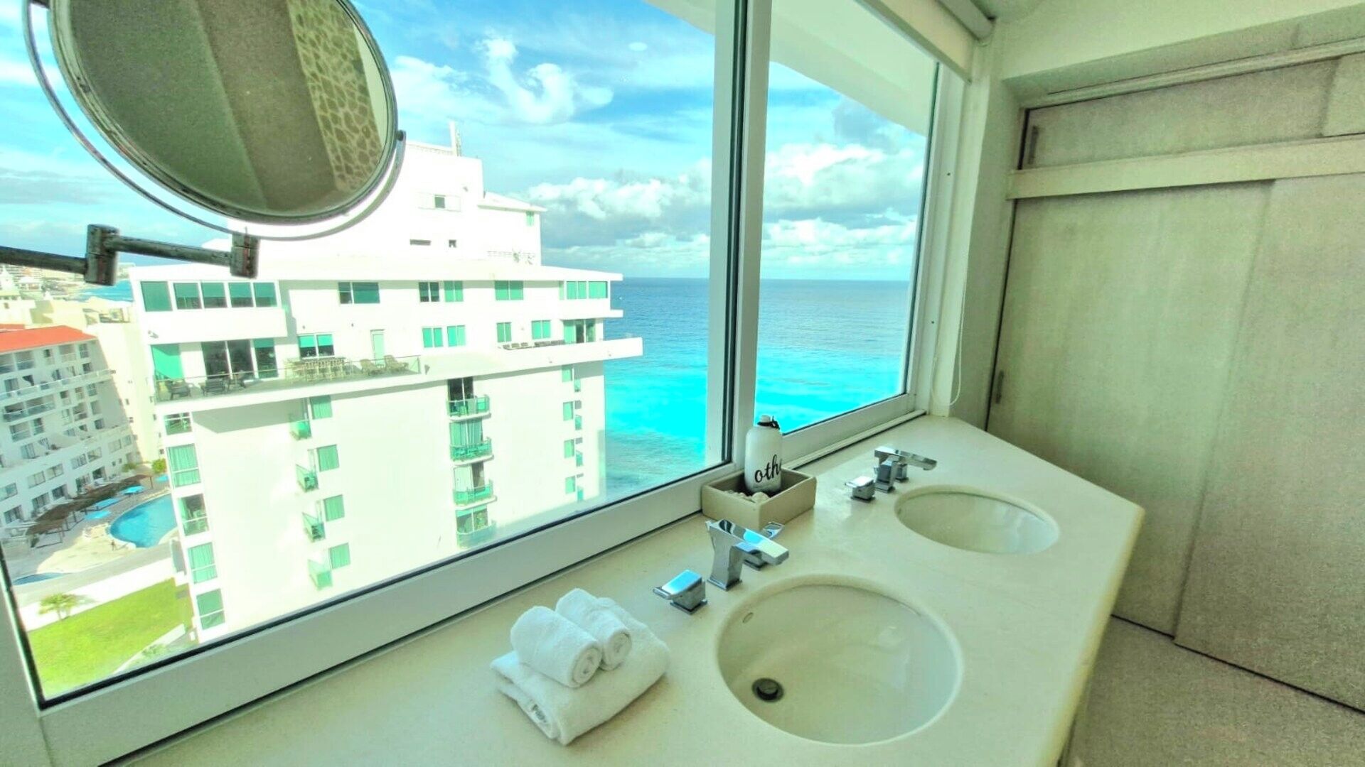 Een hotelbadkamer met twee wastafels, een grote spiegel en uitzicht op een gebouw en de oceaan.