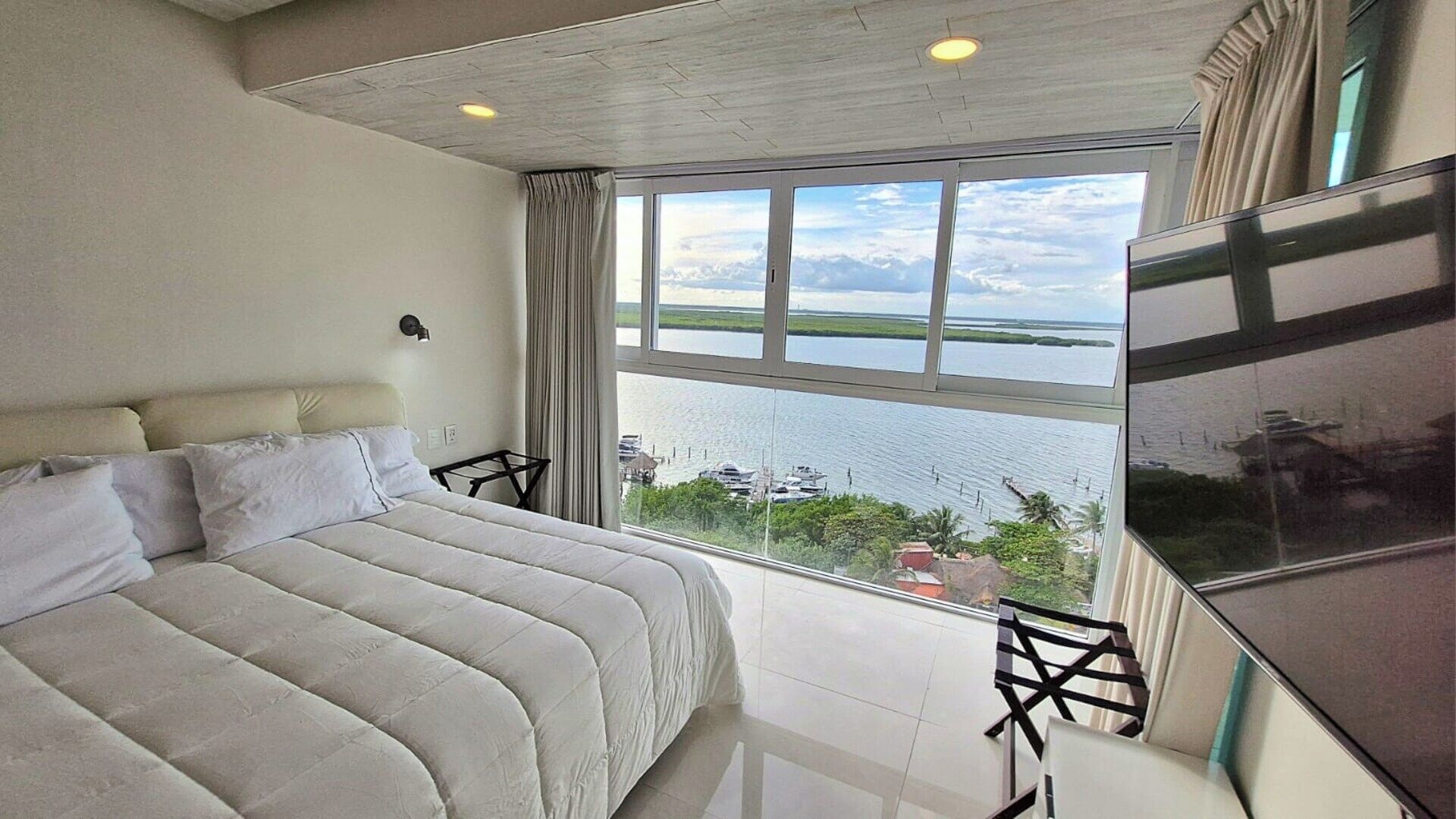 A bedroom with a large bed, a TV, and a view of a body of water.