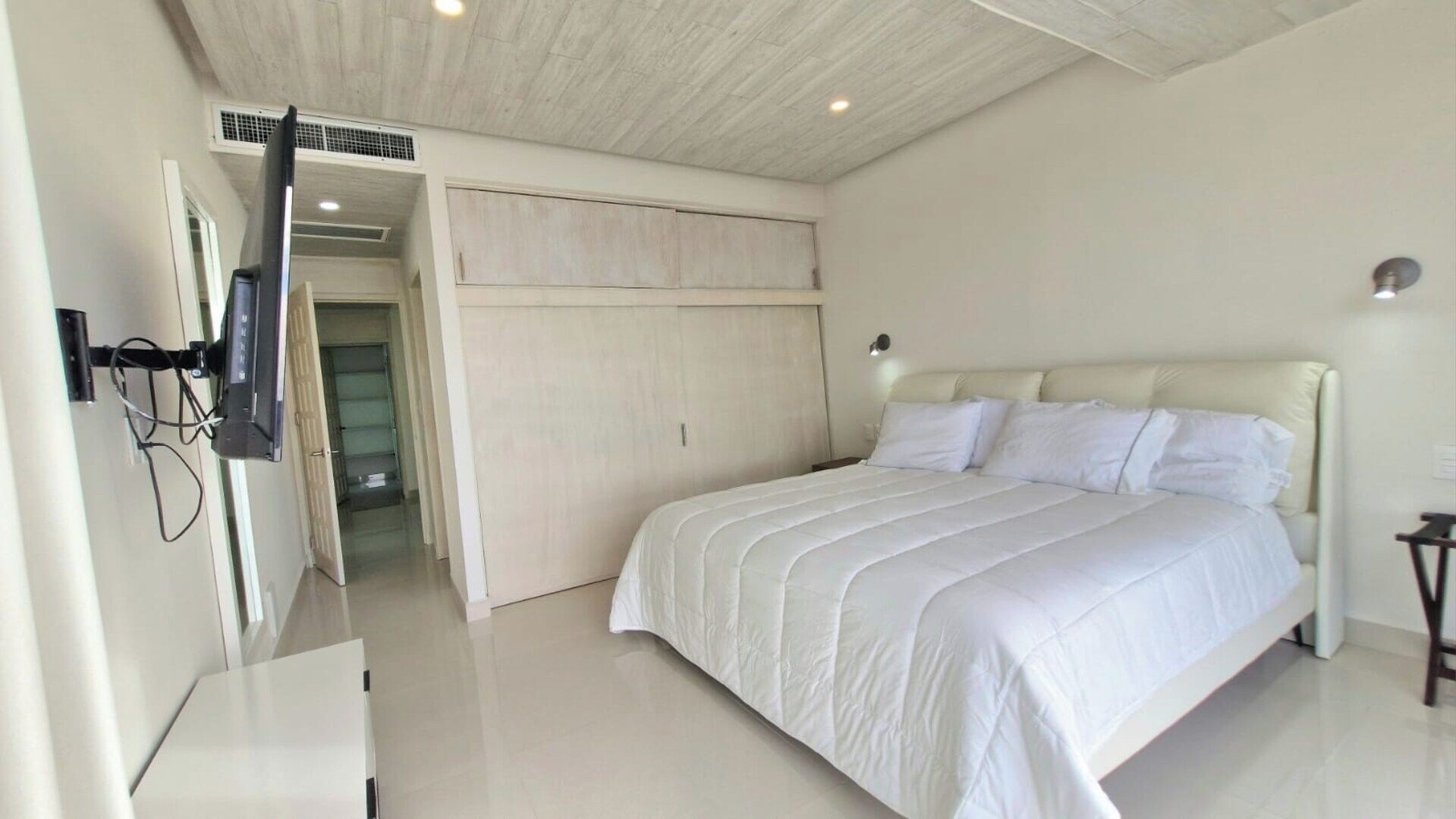 Une chambre à coucher comprenant un lit, une armoire, un téléviseur fixé au mur et une porte donnant sur une autre pièce.