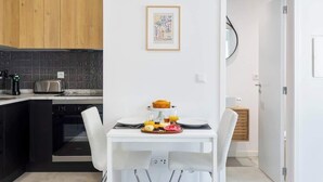 Une cuisine moderne avec un coin repas, comprenant une table blanche dressée pour le petit-déjeuner, un four noir et un meuble en bois.