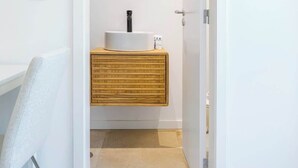 Une salle de bain avec un lavabo blanc, un meuble-lavabo en bois et un miroir rond.