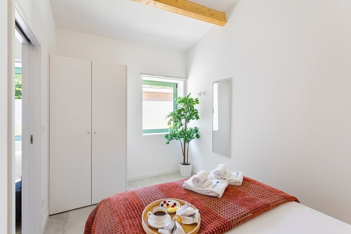 Ein Hotelzimmer mit Bett, Fenster mit Aussicht, einer Zimmerpflanze und Tablett mit Handtüchern und einer Tasse.