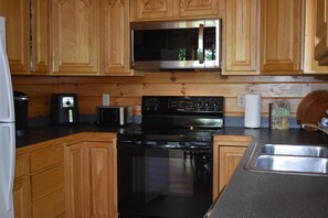 A kitchen with wooden cabinets, a stainless steel microwave, a black stove, a toaster, and a sink. - 4 bedrooms and loft sleeps 12 with view  pool table 2 levels of decks and hot tub (Sevierville)
