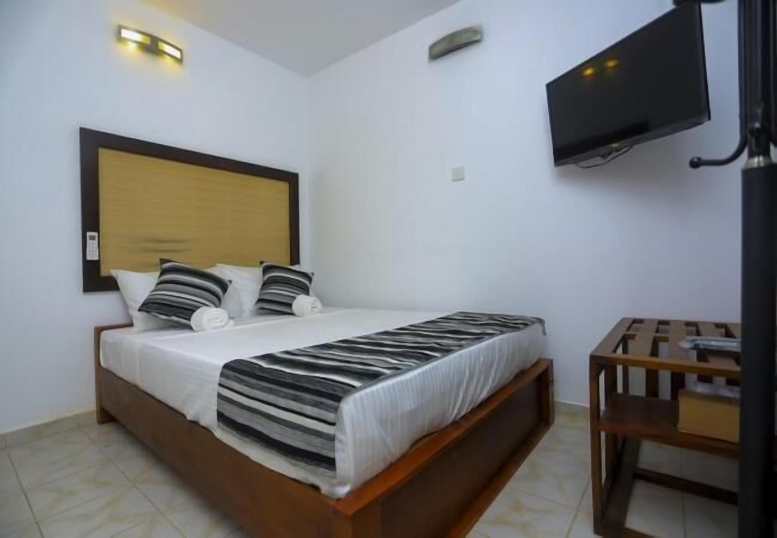 Una habitación de hotel con una cama, un televisor fijado a la pared y una pequeña mesa de madera.