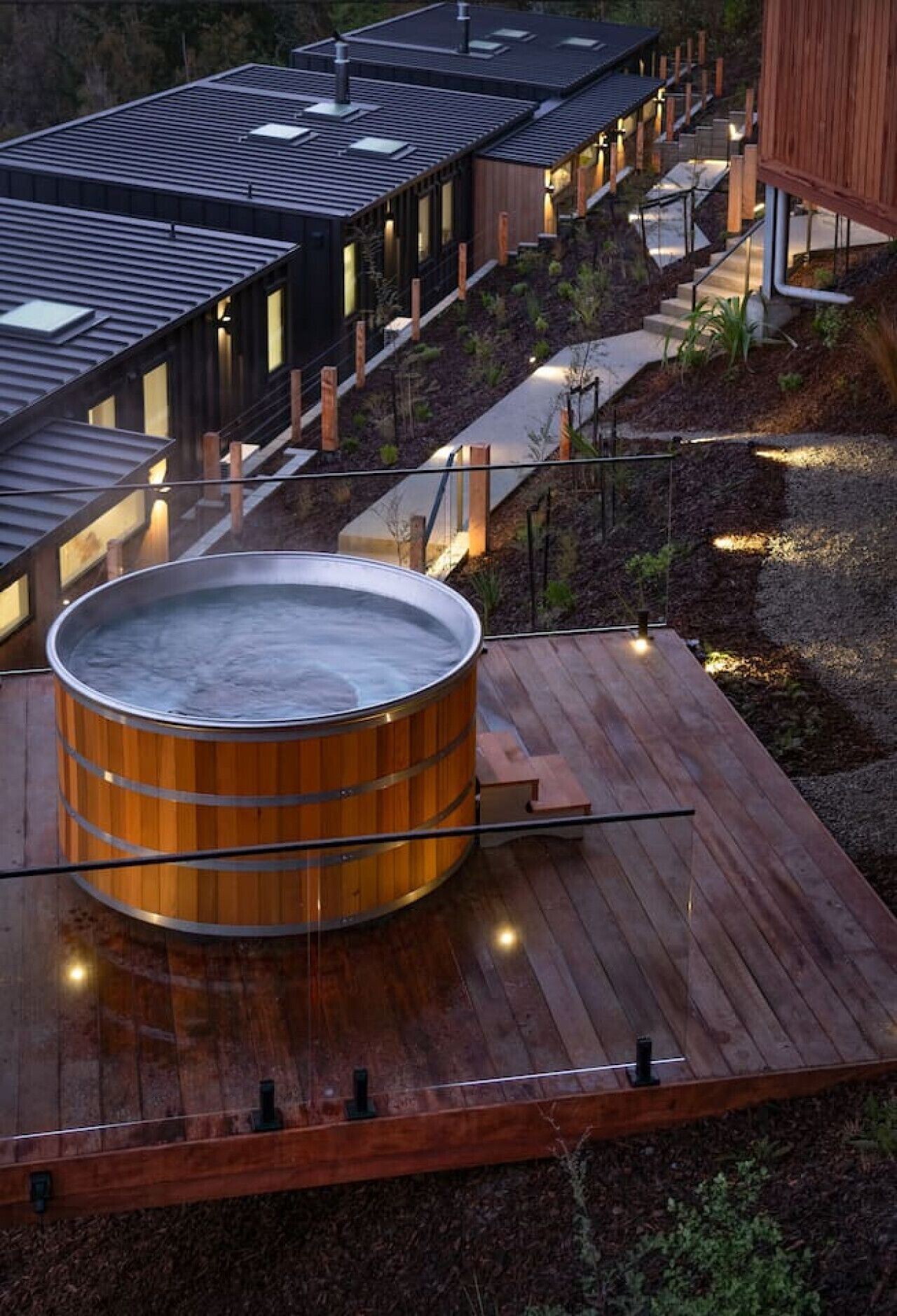 A modern building with a wooden deck, a hot tub, and a staircase leading to a second level.