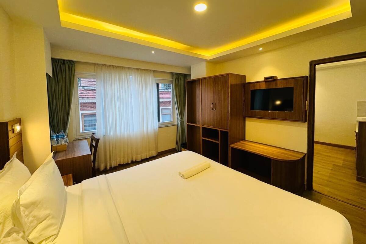 A hotel room with a large bed, a desk, a TV, and wooden cabinets.
