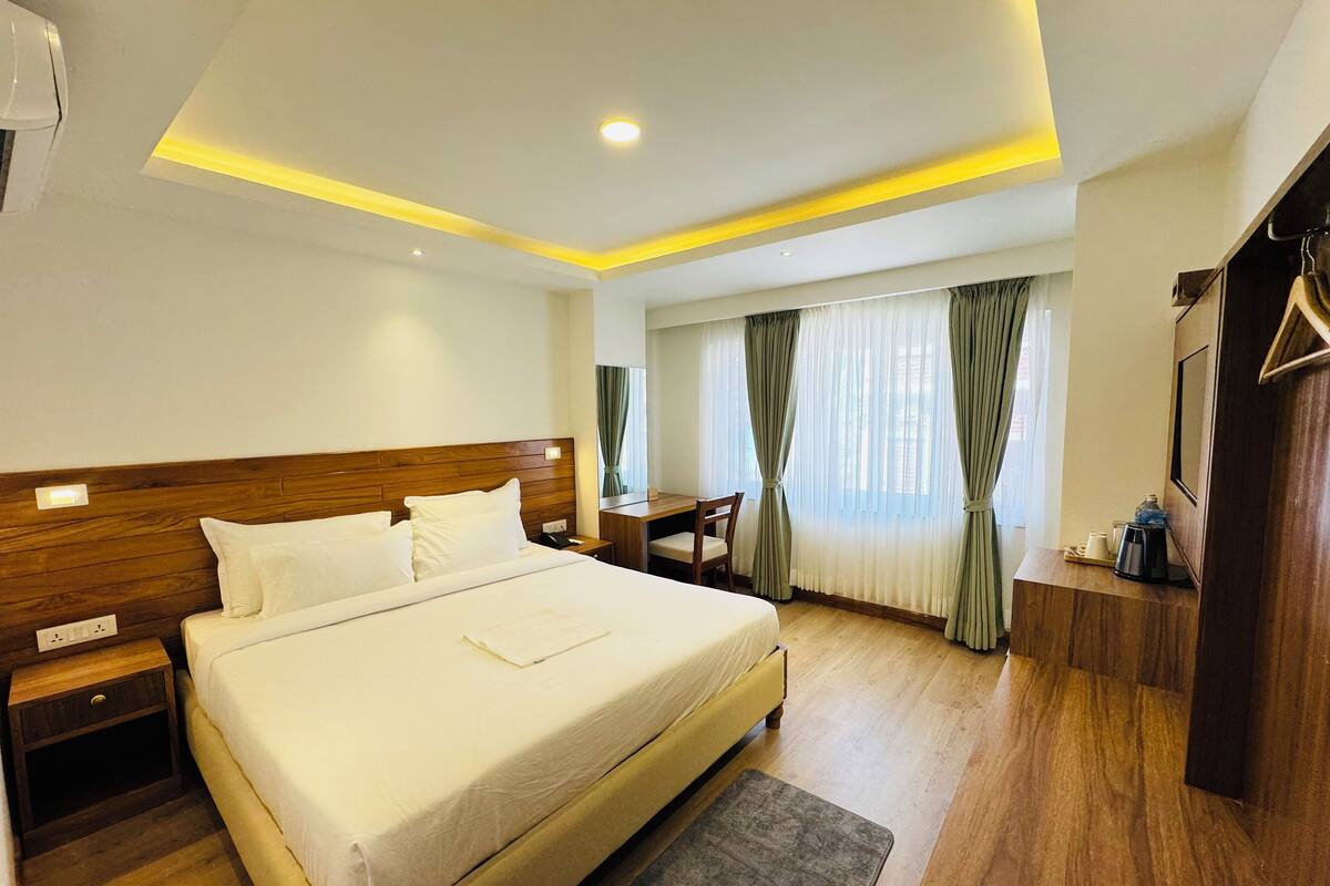 A hotel room with a large bed, wooden headboard, bedside tables, a desk, and a wardrobe.