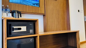 Una sala de estar moderna con un televisor montado, una cafetera y un refrigerador pequeño.