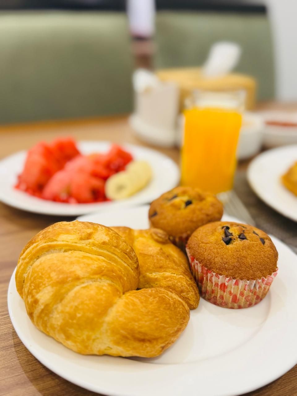 Una mesa con croissants, muffins, sandía y jugo de naranja para el desayuno.