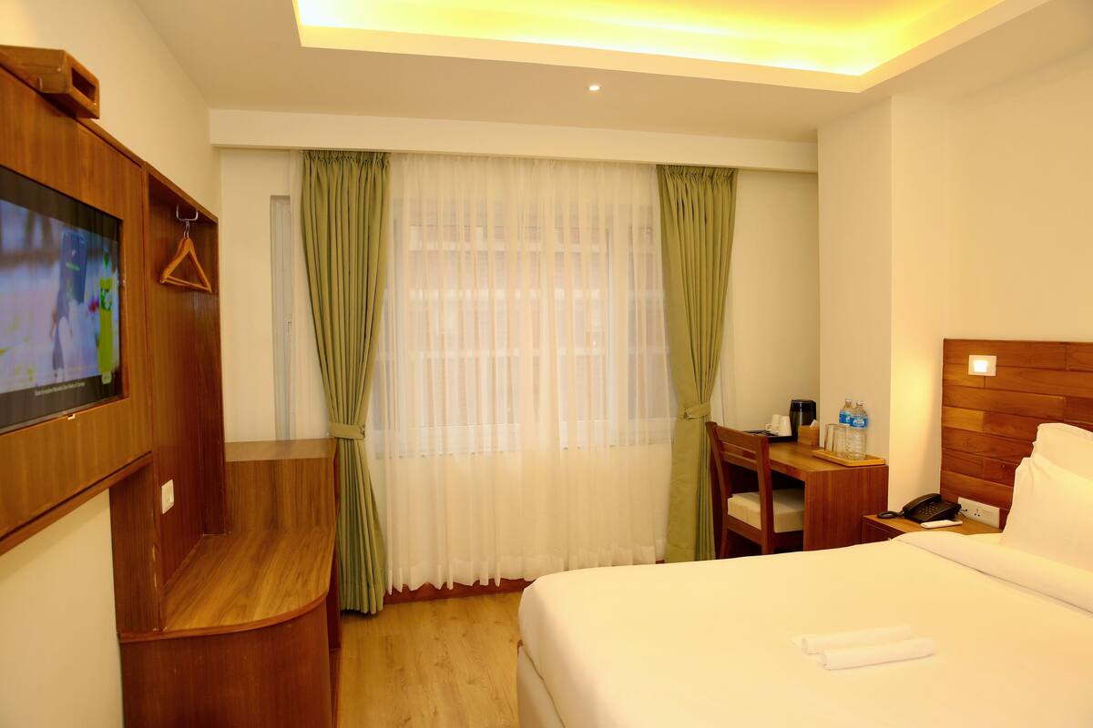 A hotel room with a bed, a desk, a television, and a window with curtains.