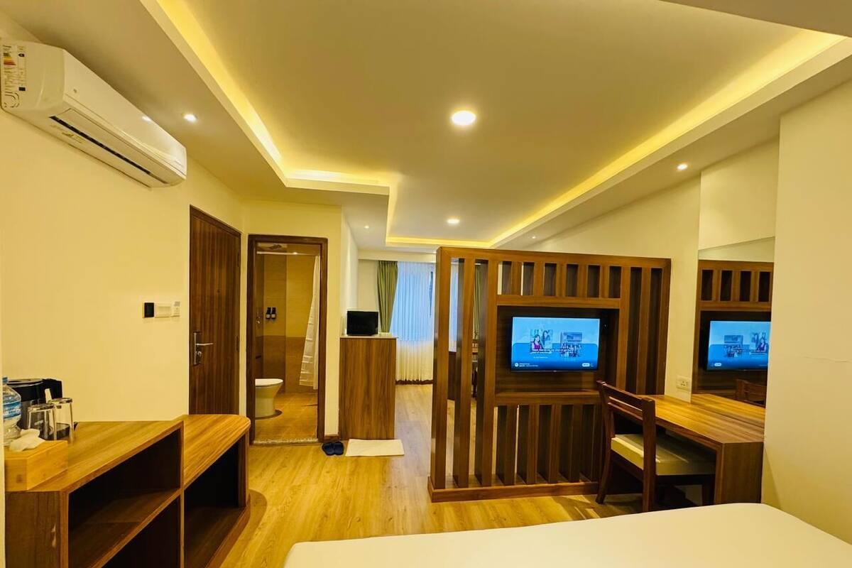 A hotel room with a bed, a desk with a chair, a TV, and a wooden partition.