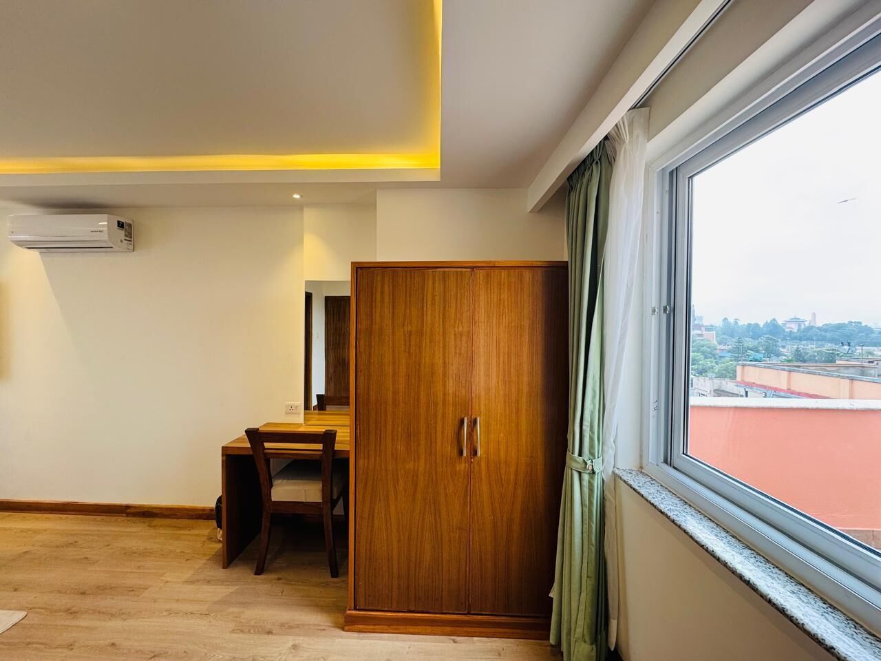 Una habitación con un armario de madera, una mesa de comedor con sillas y una ventana con vistas a edificios.