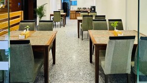 Comedor de hotel con varias mesas y sillas, una cocina al fondo y una recepción.