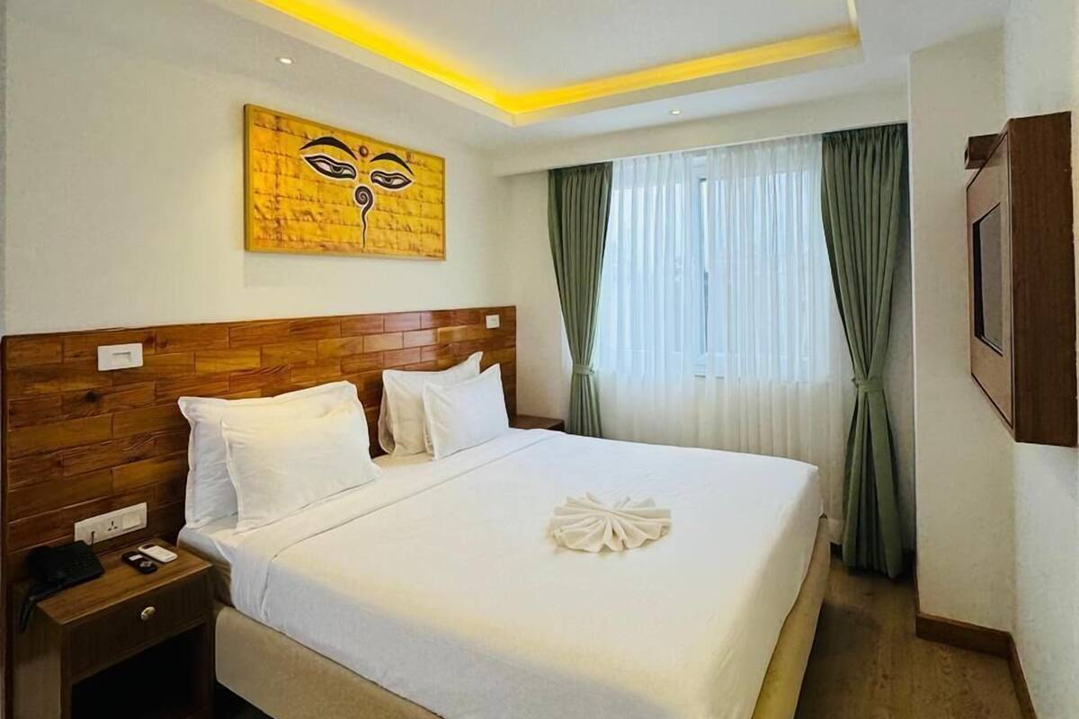 A hotel room with a wooden headboard, a large bed with white linens, a nightstand, and a wall-mounted artwork.