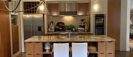 A modern kitchen with a central island, stainless steel appliances, wooden cabinets, and pendant lighting.