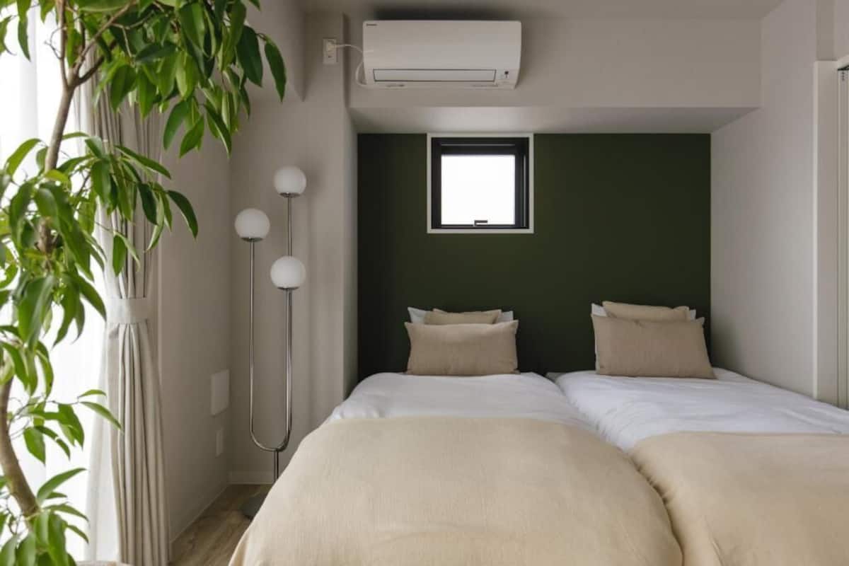 A hotel room with two beds, a window, an air conditioning unit, and a floor lamp.