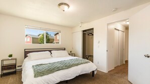 A bedroom with a bed, a nightstand, a window, and a door leading to another room. - Spacious 2BR Duplex Family Group Friendly (Lynnwood)