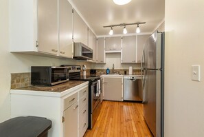 A compact kitchen with white cabinets, a microwave, a stove, a dishwasher, and a refrigerator. - Spacious 2BR Duplex Family Group Friendly (Lynnwood)