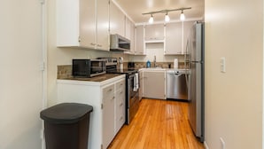 A compact kitchen with white cabinets, a microwave, a dishwasher, and a stainless steel refrigerator. - Spacious 2BR Duplex Family Group Friendly (Lynnwood)