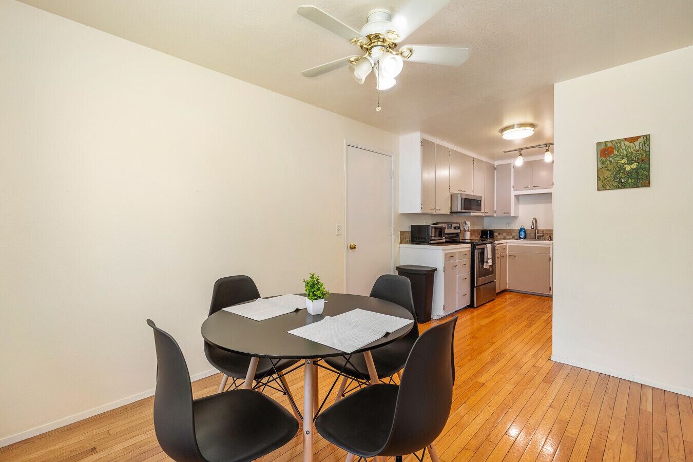 A compact living space with a dining area featuring a round table and four chairs, a kitchenette with modern appliances, and a ceiling fan.
