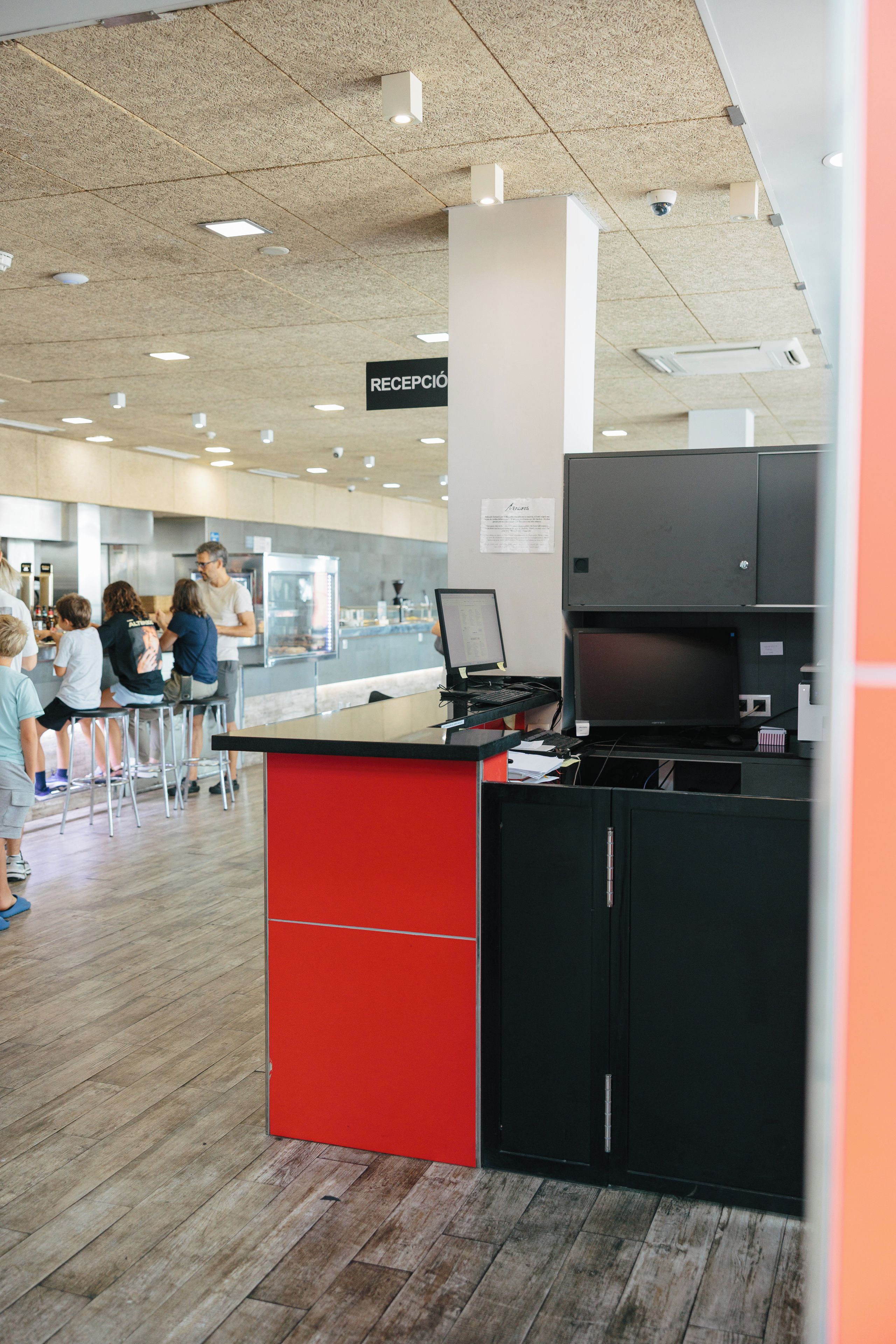 A reception area with a sign indicating 'RECEPCIÓN', a counter with a computer, and a group of people in the background.