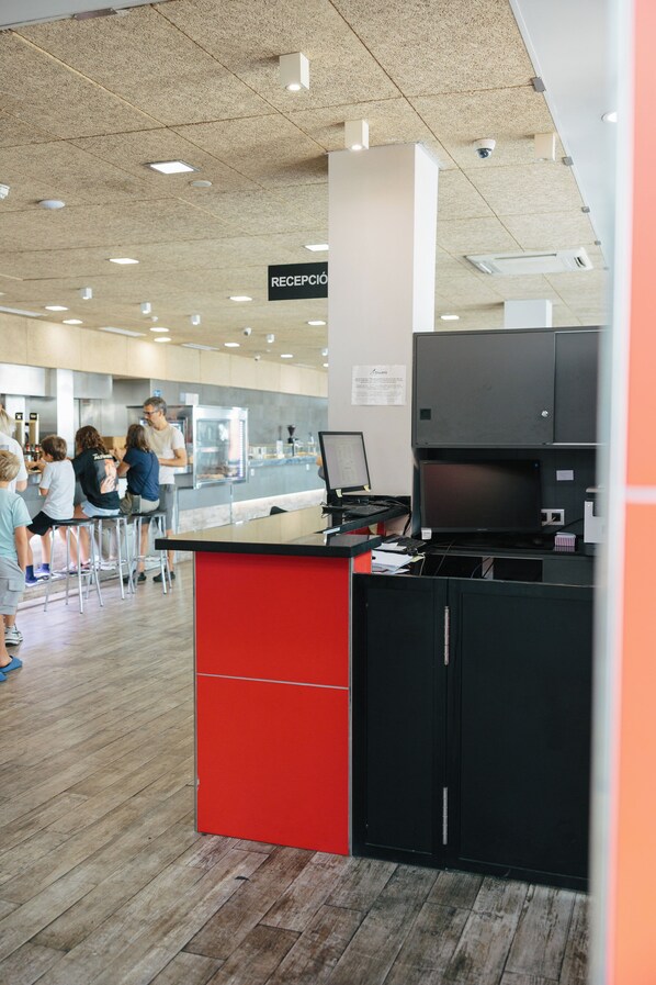 A reception area with a sign indicating 'RECEPCIÓN', a counter with a computer, and a group of people in the background. - As El Puig (Puig)