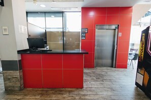 A reception desk with a red tiled wall, a closed elevator, and a sign indicating the hotel name.
