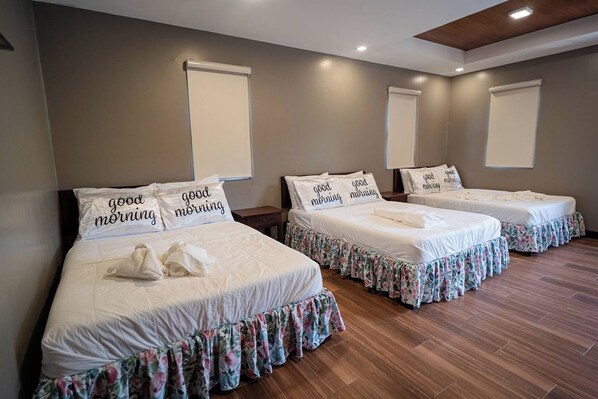 A hotel room with three beds, each with floral bed skirts and pillows with 'good morning' text.