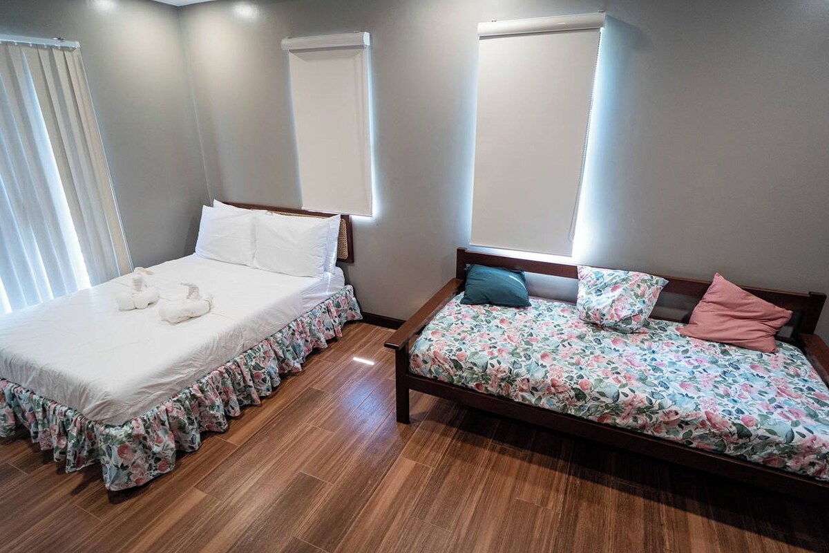 A bedroom with two beds, one with a floral bedspread and the other with a plain white bedspread.