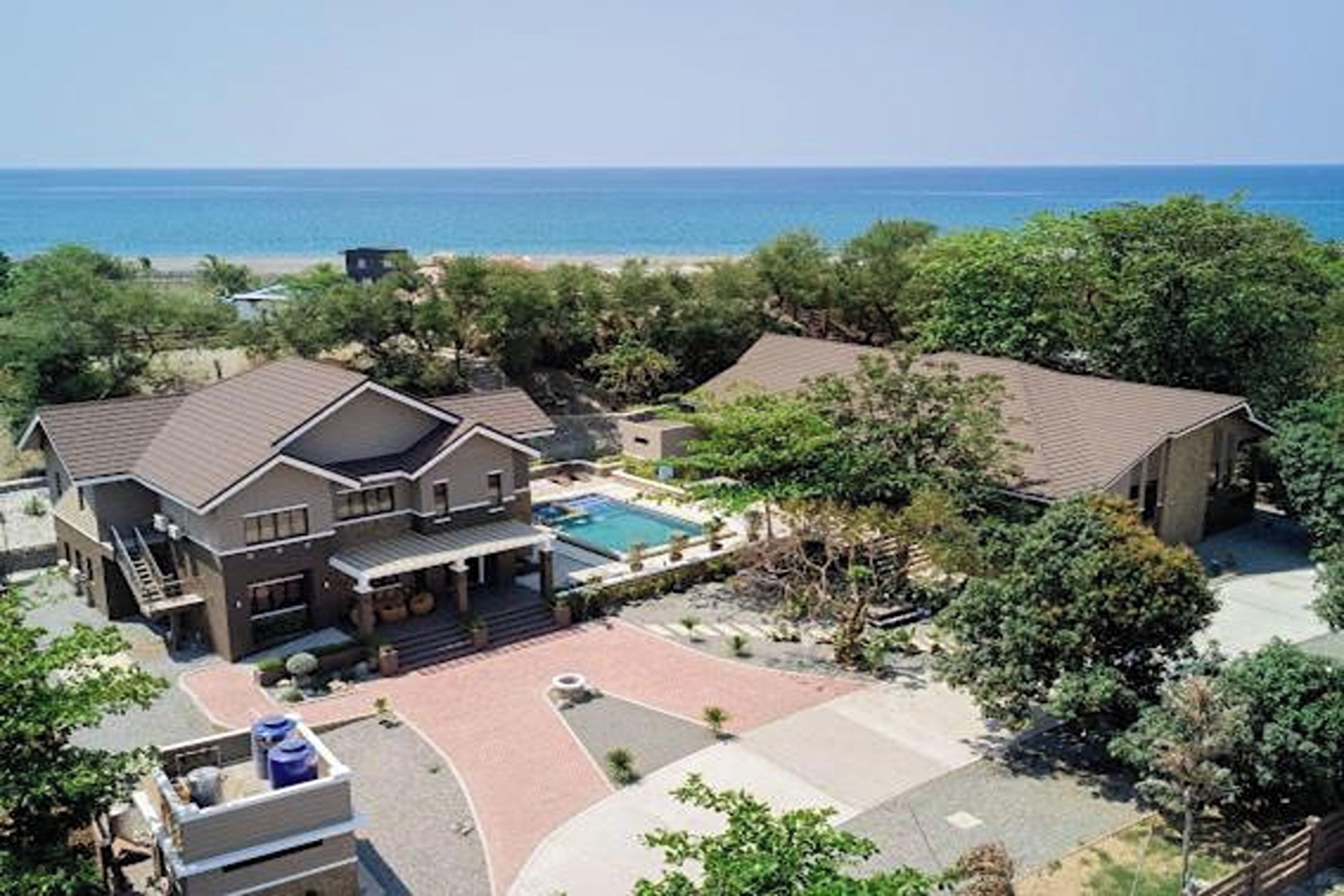 A residential property with a swimming pool, multiple buildings, and a view of the ocean.