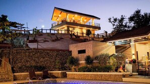 Area piscina con muro in pietra, una poltrona da relax e un edificio con un balcone.