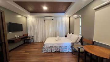 A hotel room with a bed, a desk, a chair, a TV, and a window with curtains.