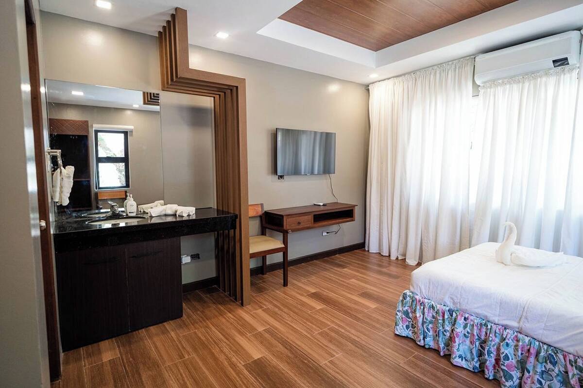 A hotel room with a wooden floor, a large mirror, a flat-screen TV, a bed with a floral skirt, and a desk with a chair.