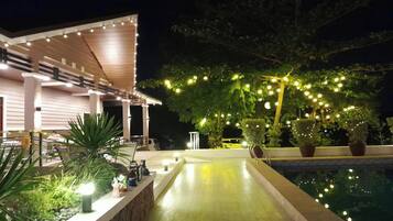 An outdoor pool area with a wooden deck, potted plants, and string lights.