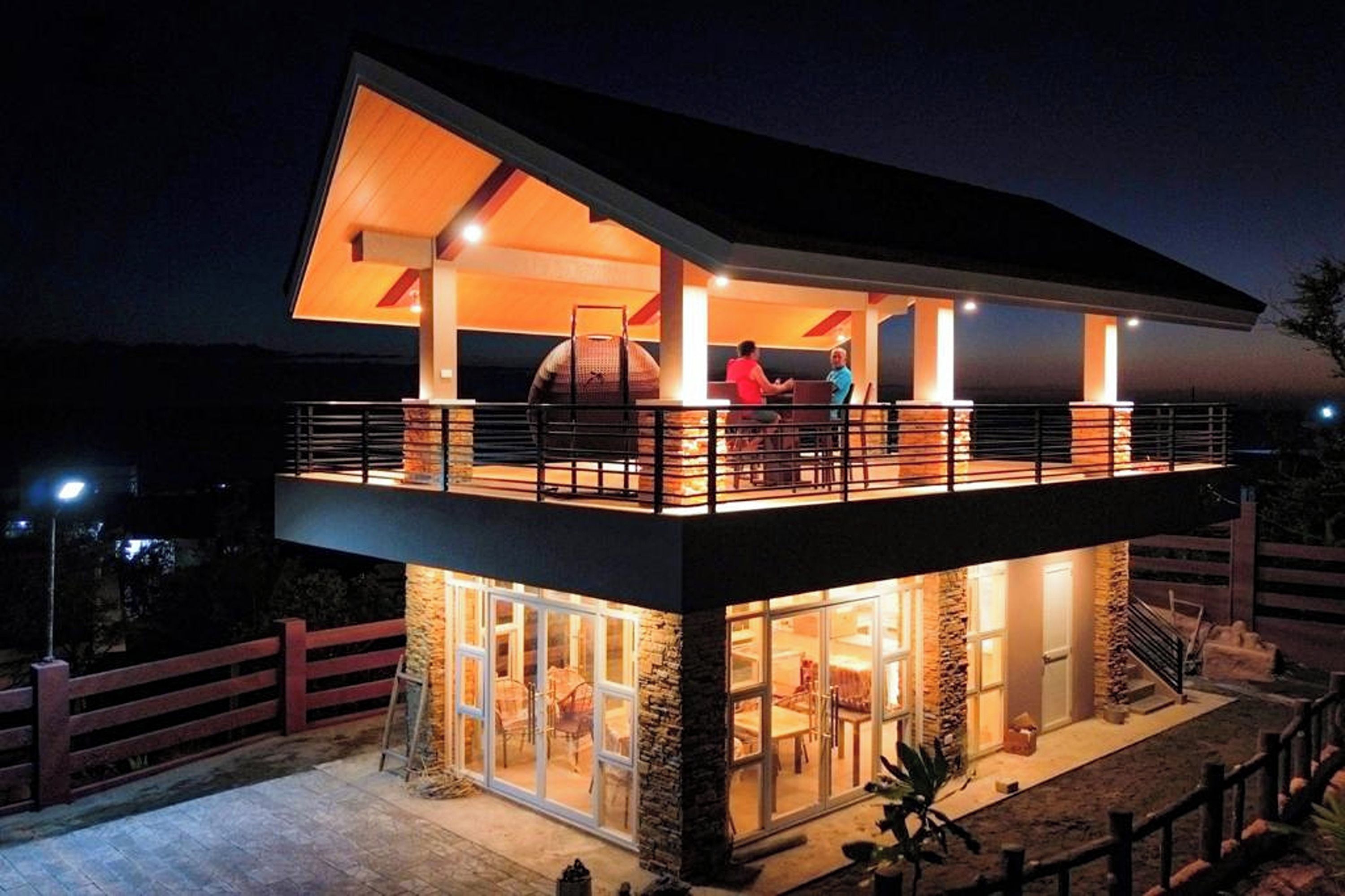 A two-story modern house with a balcony, large windows, and a stone exterior.