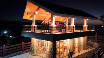 A two-story modern house with a balcony, large windows, and a stone exterior.