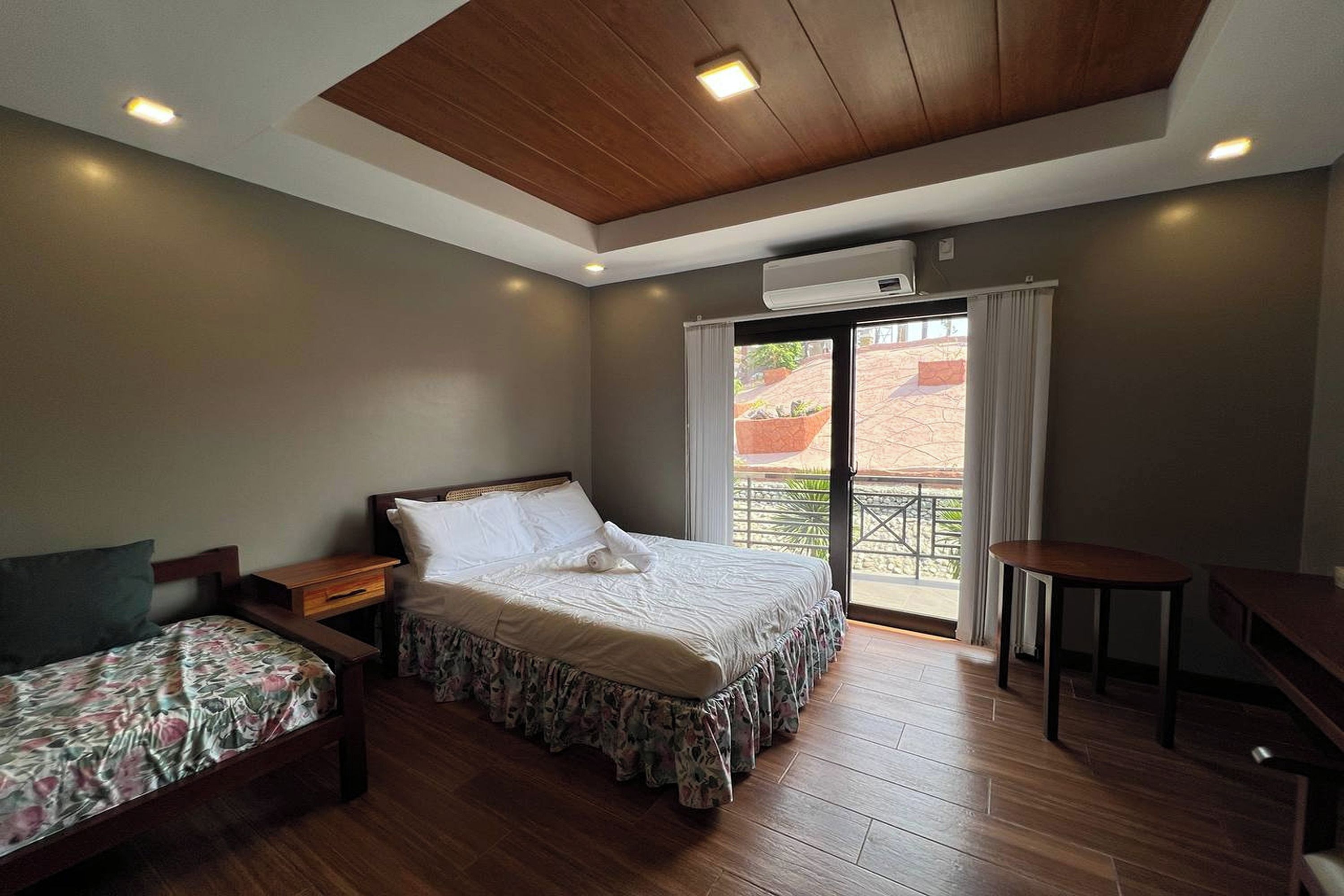 A bedroom with a bed, a smaller bed, a desk, and a window with curtains.