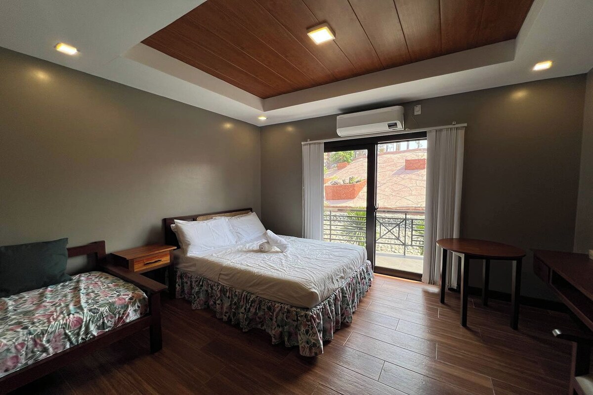 A bedroom with a bed, a smaller bed, a desk, and a window with curtains.