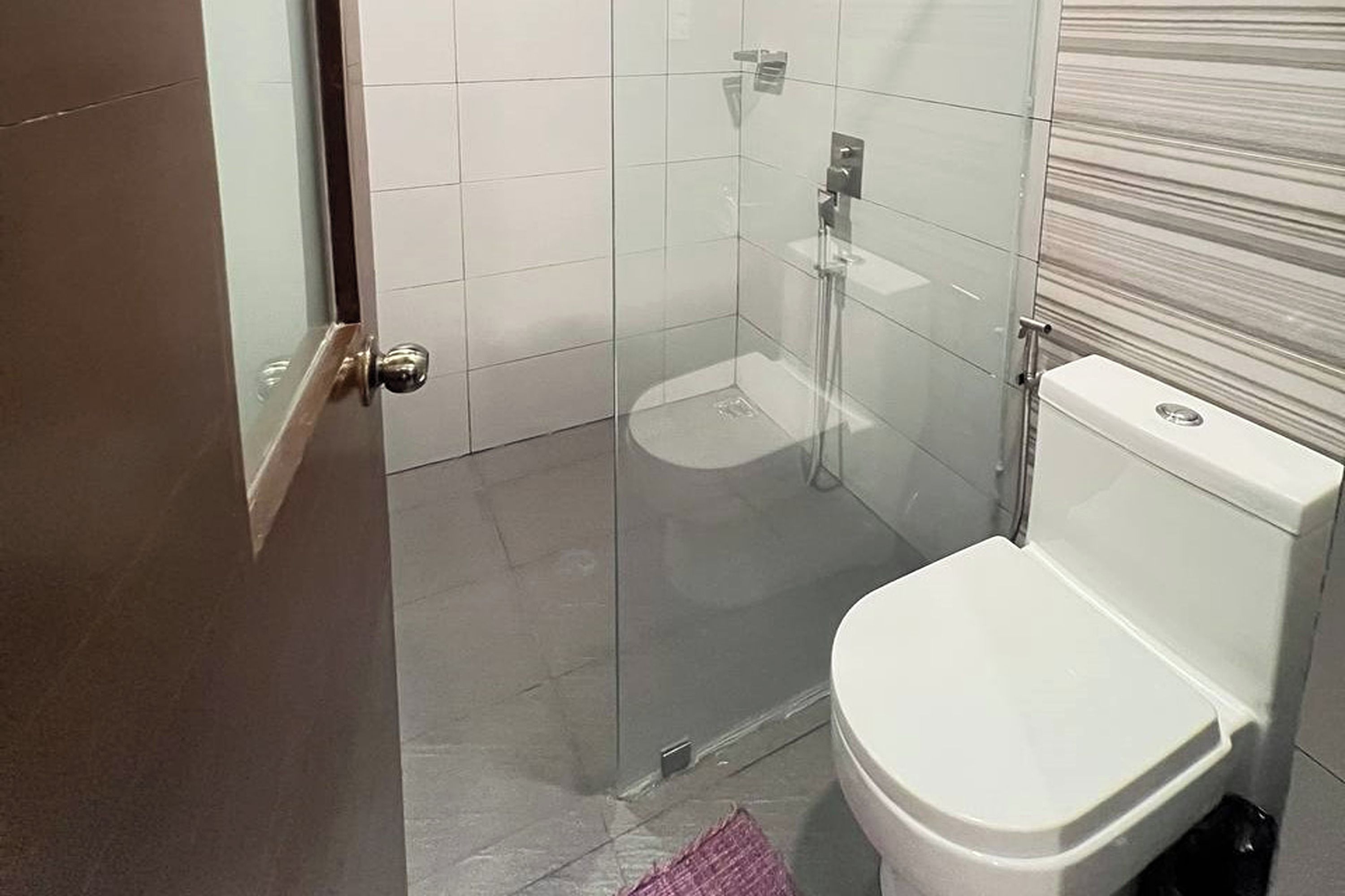 Ein Badezimmer mit Duschkabine aus Glas, einer weißen Toilette und einem gefliesten Boden.