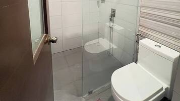 Ein Badezimmer mit Duschkabine aus Glas, einer weißen Toilette und einem gefliesten Boden.